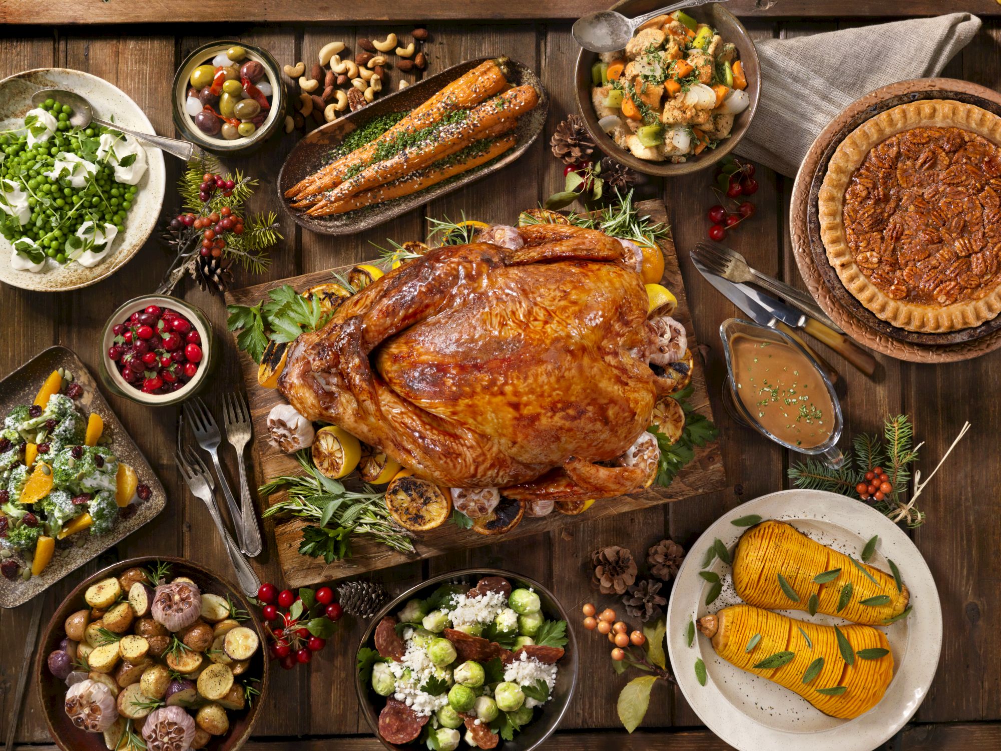 A festive feast spread&mdash;roasted turkey and sausages, salmon and pie, with salads, olives, nuts, veggies, and sauces on rustic boards.