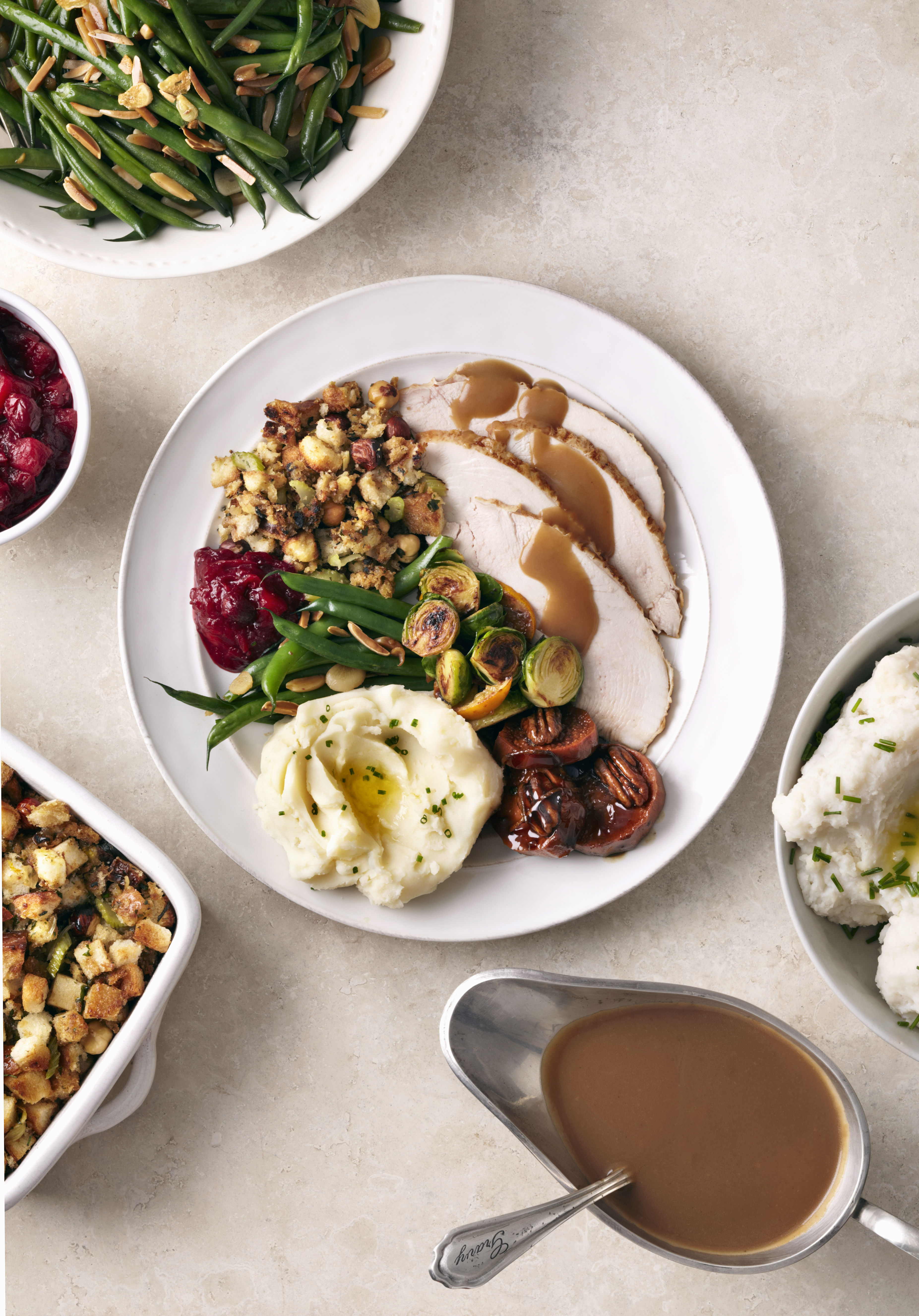 A plated roast turkey dinner with mashed potatoes, gravy, stuffing, Brussels sprouts, green beans, and cranberry sauce.