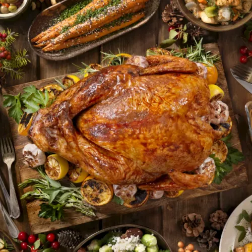 A holiday feast: a roasted turkey on a wooden board, surrounded by herbs, garlic, mushrooms, veggies, and gravy.
