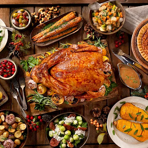 A festive holiday table with a roasted chicken/turkey, baked pie, salmon, vegetables, salads, olives and herbs.