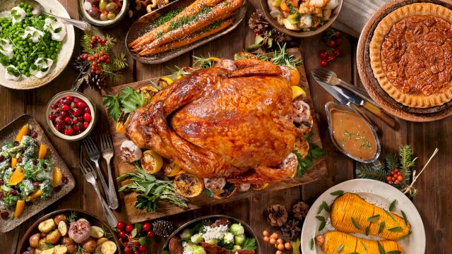 A festive holiday table with a roasted chicken/turkey, baked pie, salmon, vegetables, salads, olives and herbs.