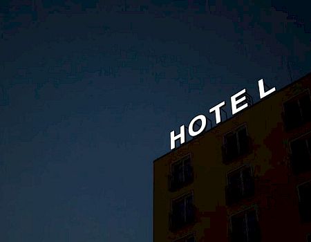 A building with a partially lit "HOTEL" sign against a dark sky, missing the letter "L".