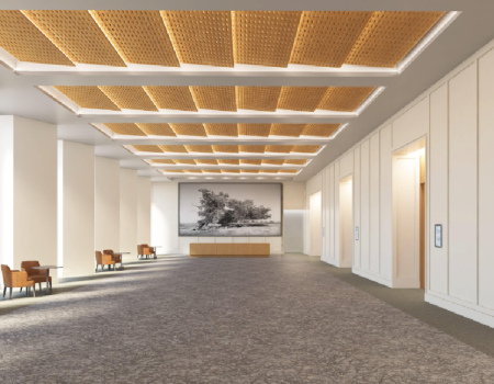 A spacious, modern lobby with high ceilings, warm wood ceiling panels, gray carpet, white walls, seating along the sides, and a reception desk at the far end.