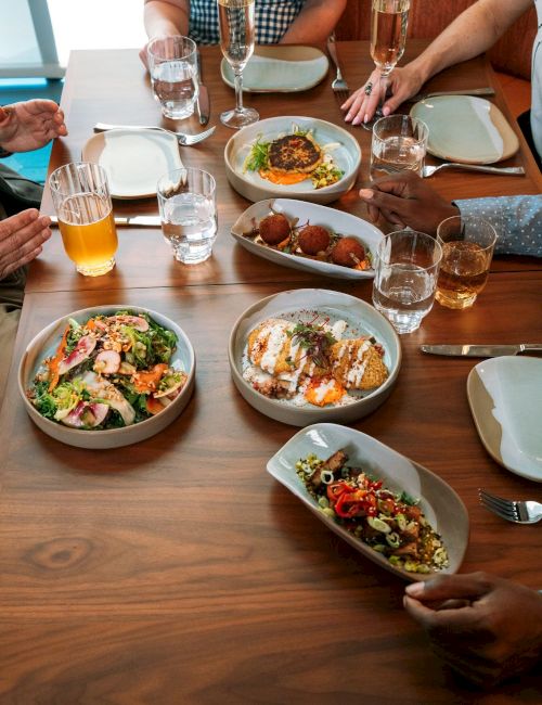 Friends dine at a wooden table with gourmet plates and glasses of juice and champagne.