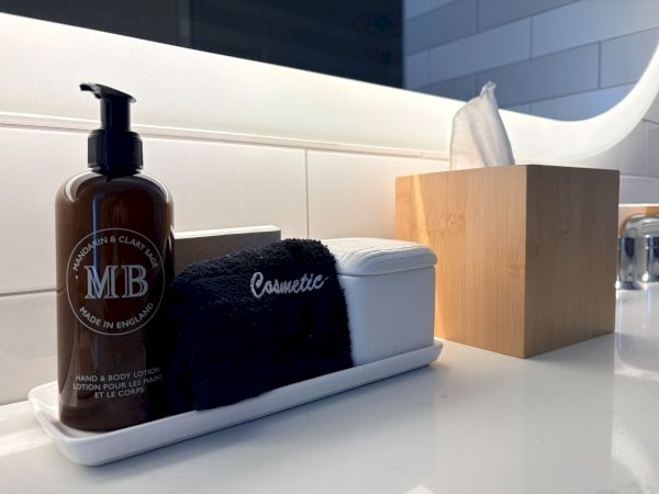 A bathroom vanity with a hand & body lotion pump, folded towels, tissue box, and a bin of toiletries.