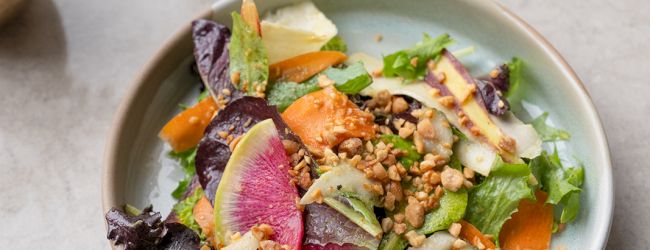 A colorful salad bowl with mixed greens, sliced beets, carrots, apples, and crunchy nuts, topped with a light vinaigrette.