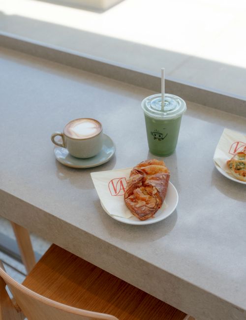 A coffee cup, a green smoothie, and a slice of pizza sit on a cafe table.