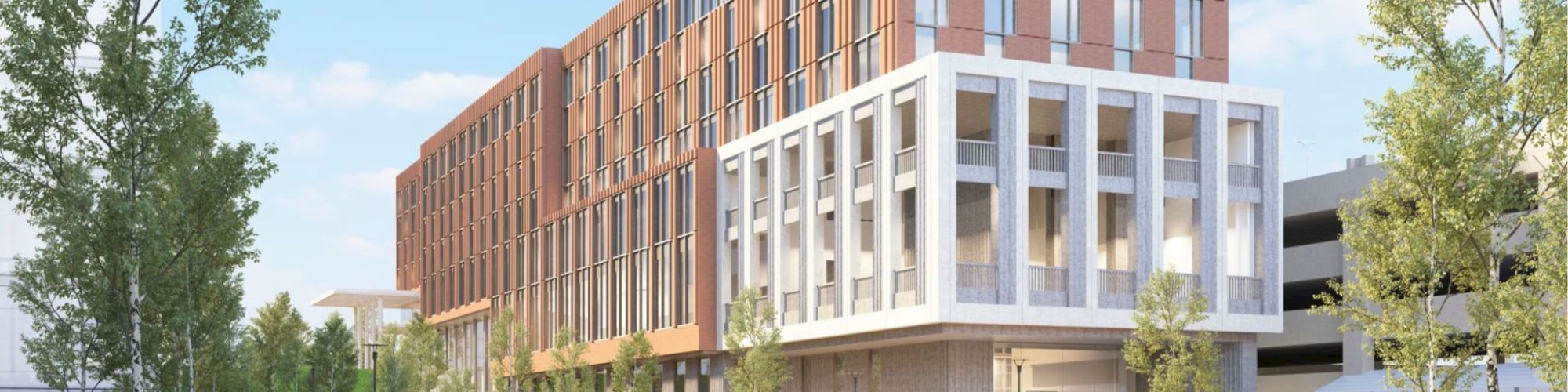 A modern mixed-use building with white and copper-toned facades, large windows, and a glassy ground level, set beside a water feature and trees.