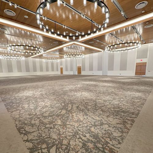 An empty event hall with patterned carpet and rows of hanging light fixtures mounted on a wood ceiling.
