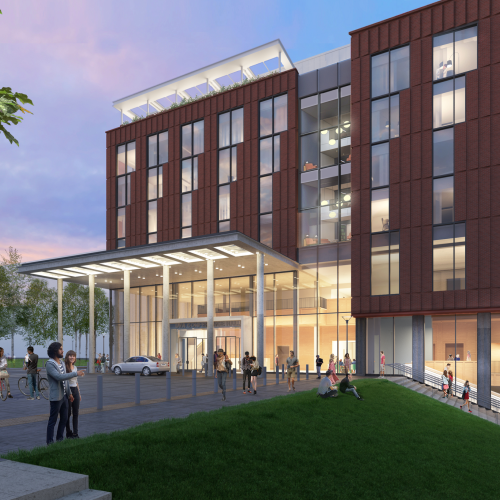 A modern multi-story building with glass windows, brick facade, a covered entrance, people gathered outside, and a green lawn area.