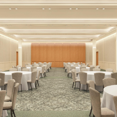 A spacious conference room with round tables and beige chairs, arranged in rows, leading to a wooden stage at the far end.