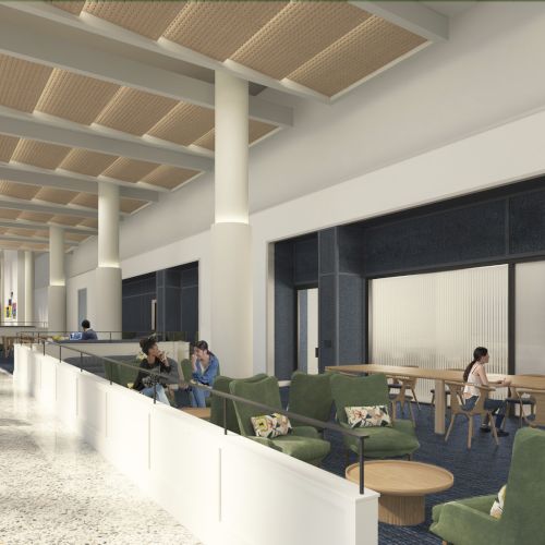 A modern, open lounge with white walls, tall windows, and a spacious seating area featuring green chairs, round tables, and people working and chatting.