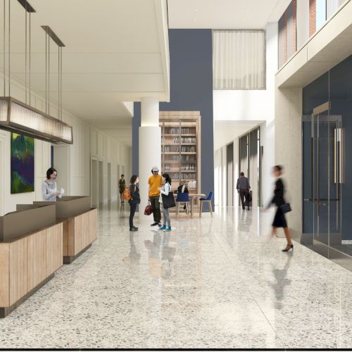 A modern office lobby with a front desk, polished floors, glass walls, and people walking through the bright, open space.
