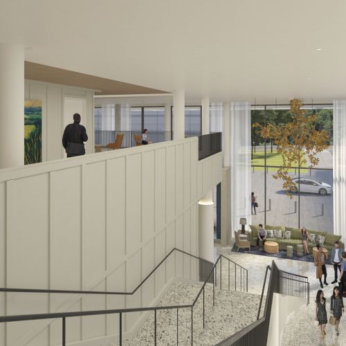 A modern, bright lobby with a mezzanine, white walls, tall windows, stairs down to a spacious reception area, and people walking and chatting.