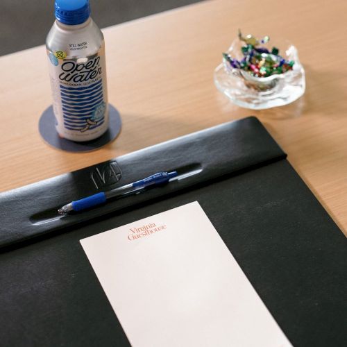 A meeting table with a bottle of One Water, a pen on a notebook, and a small glass bowl of colorful candies.