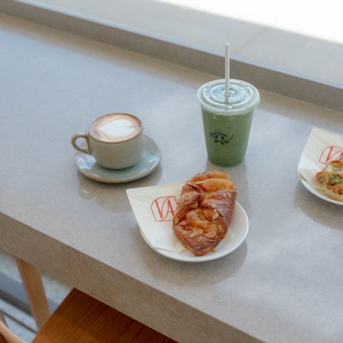 A caf&eacute; table with a latte cup, a green iced drink, and an almond croissant on a plate.