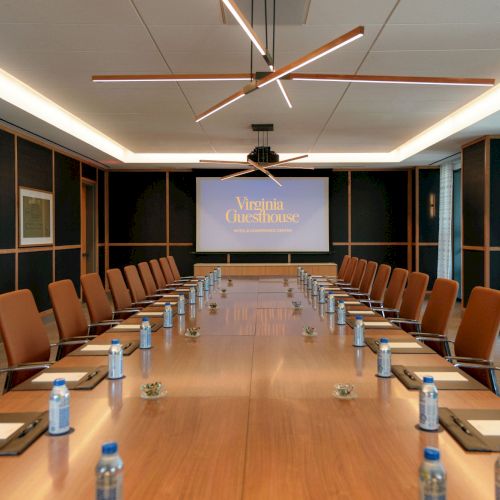 Conference room with a long table of water bottles, orange chairs, and a &ldquo;Virginia Guesthouse&rdquo; presentation screen at the front.