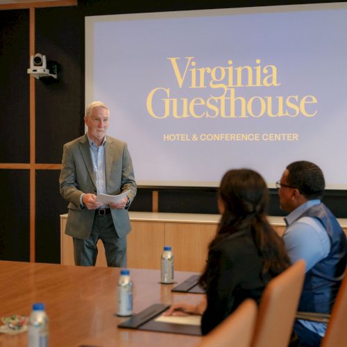 A speaker presents at &ldquo;Virginia Guesthouse&rdquo; Hotel & Conference Center, addressing an audience in a meeting room.