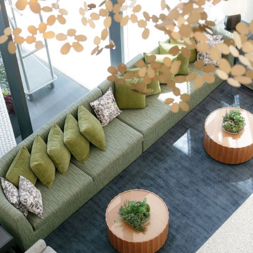An indoor lounge with a green sofa, pillows and small wooden tables, decorated with hanging paper flower cutouts.