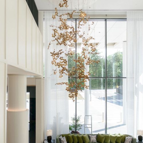 A bright modern living room with a green sectional sofa and a gold petal-like chandelier hanging above the seating.