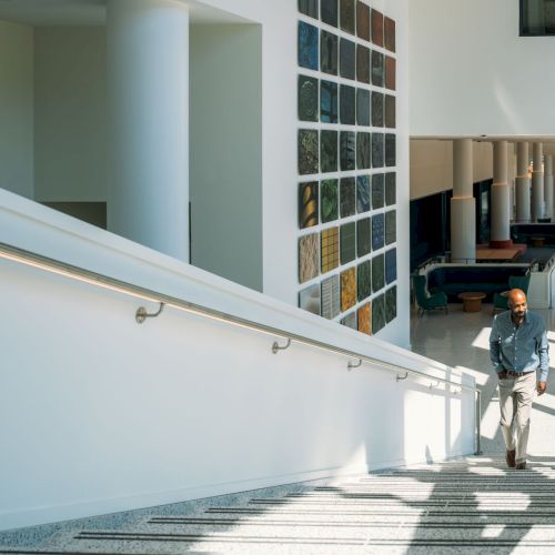 A couple walks down a bright modern stairwell lined with colorful art panels and columns.