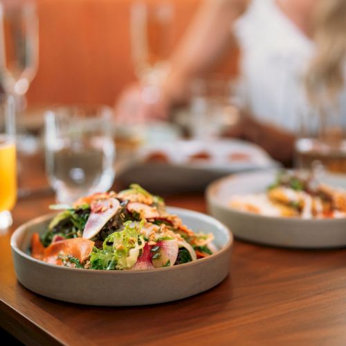 A dining table set with a salad bowl, other dishes in the background, and juice glasses for a shared meal.
