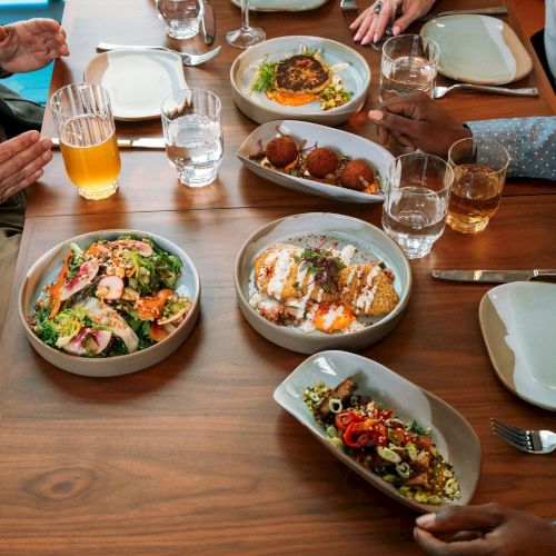 A group dining at a restaurant table with plates of food and glasses of drinks, everyone about to eat.