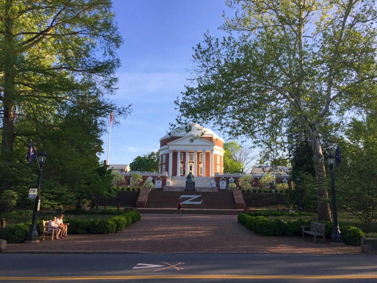 A classical domed monument with steps, flanked by trees and lamp posts, set in a serene park-like plaza.