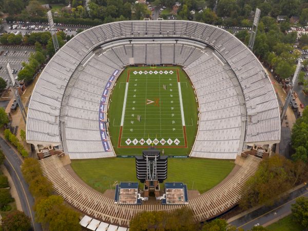 An aerial view of a large football stadium with a green field, seating all around, and a few structures/advertisements along the sides, ending this sentence.