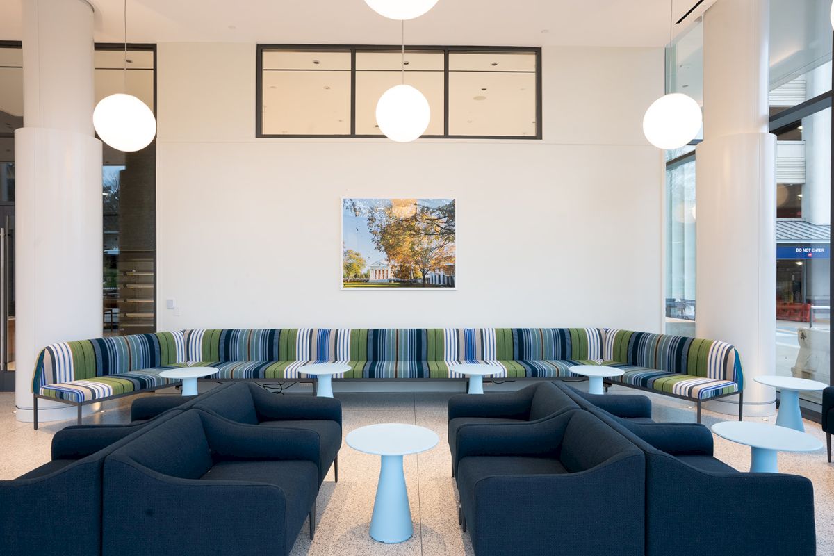 Bright office lounge with blue sofas, a striped banquette, round white lamps, and small white side stools.