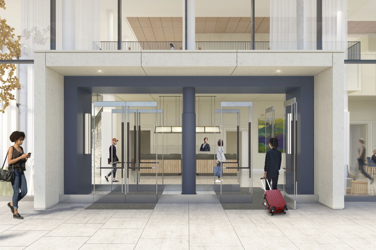 People entering and exiting a modern building lobby with glass doors; a traveler with a red suitcase stands outside as others walk in and out.