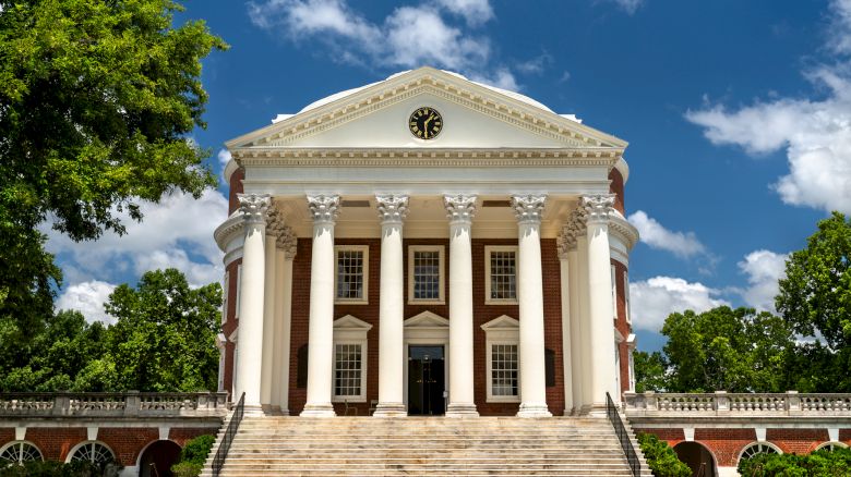 A grand white neoclassical building with tall columns, a triangular pediment, and wide steps, set in a sunny park with trees.