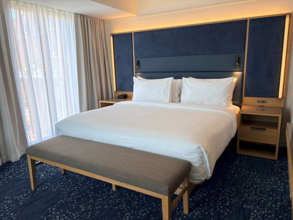 A hotel-style bedroom with a large bed, white linens, bedside tables, and a blue upholstered headboard with warm lighting.