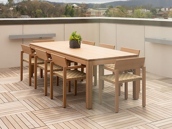 A rooftop deck with a wooden dining table and six chairs, potted plant centerpiece, overlooking a cloudy sky and distant hills.