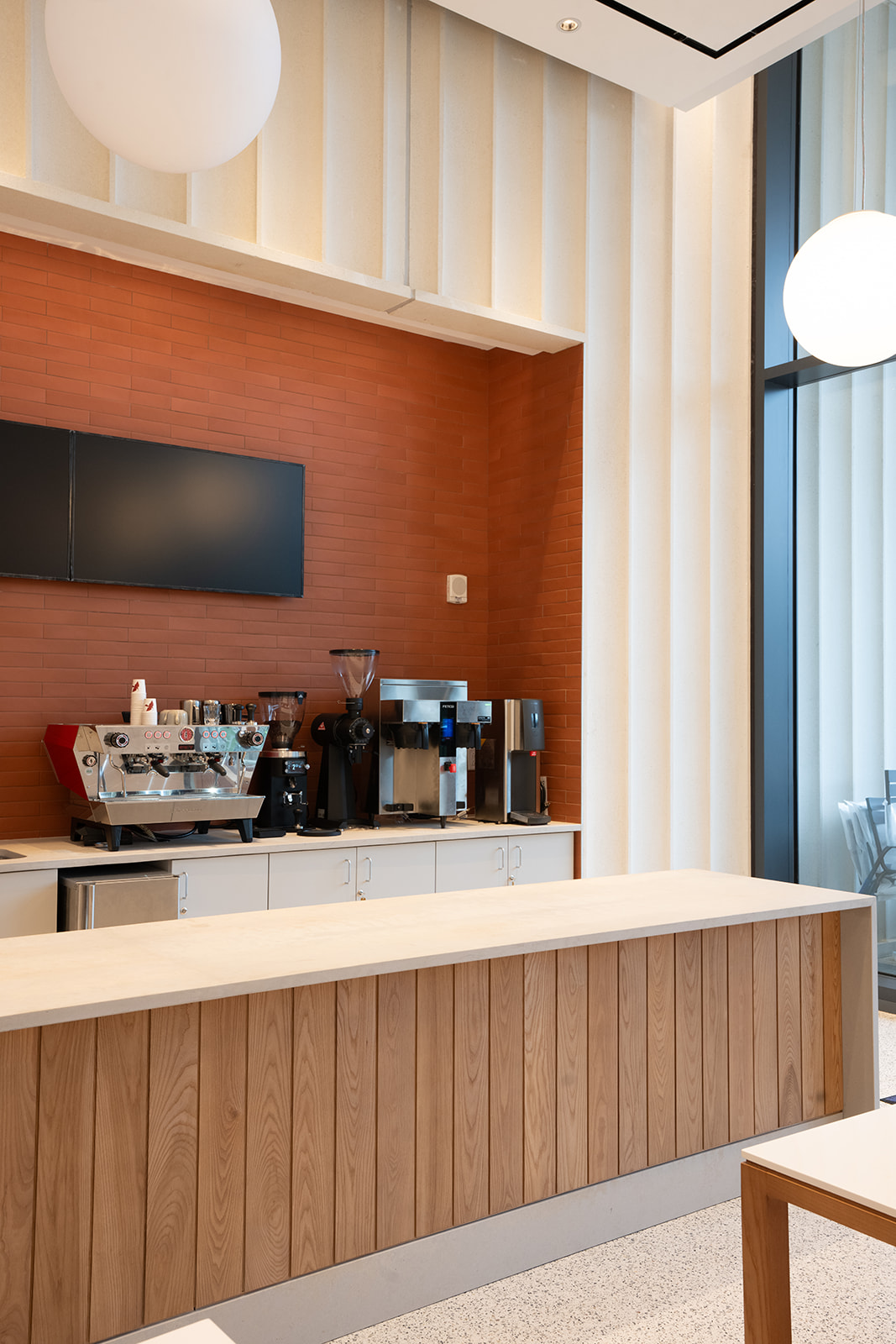 A modern cafe counter with a coffee station, wood paneling, and a high windowed wall, creating a bright, minimalist setting.