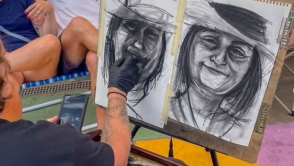 A man sketches a dual portrait on an easel, while others chat nearby; art supplies and a bright, patterned outdoor space surround them.