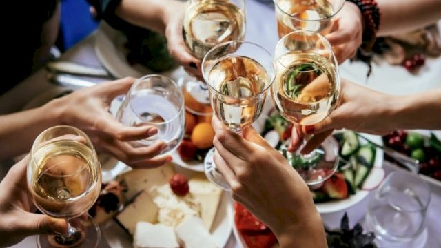 A group toasting with champagne flutes over a festive table of assorted foods and desserts, celebrating together.