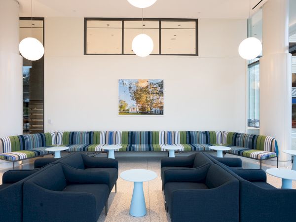 A modern lounge with blue sectional seating, striped bench, small tables, pendant globe lights, and a landscape wall photo.