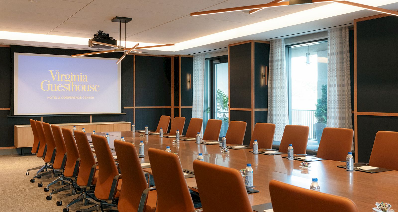 Conference room at the Virginia Guesthouse hotel, with a projection screen, orange chairs, and bottled water on a meeting table.