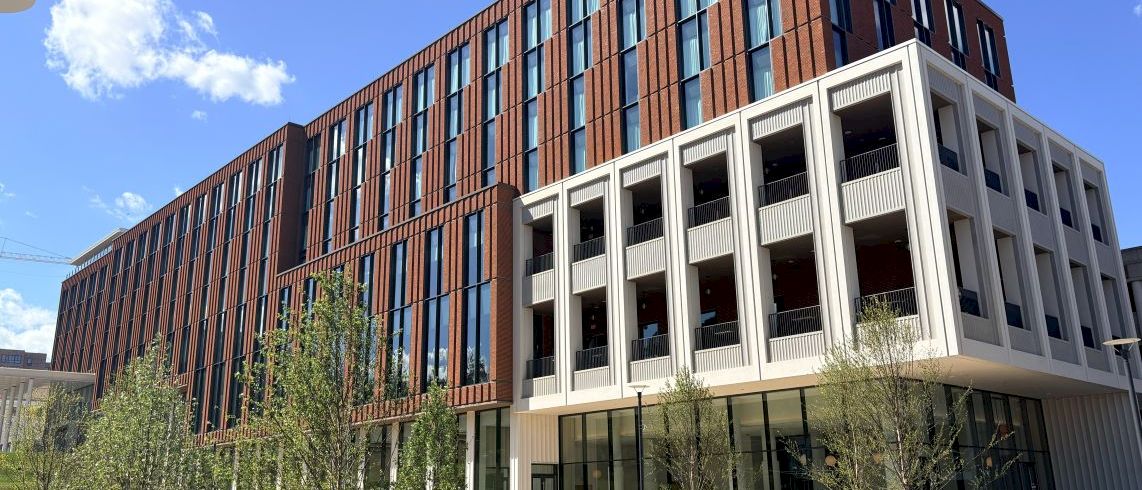 A modern red-brick and glass office building with white balconies, set against a clear blue sky.