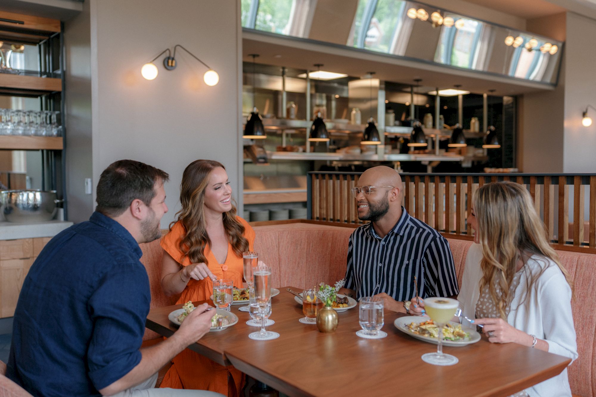 A group of friends is dining and toasting with drinks at a restaurant table, smiling and chatting together.
