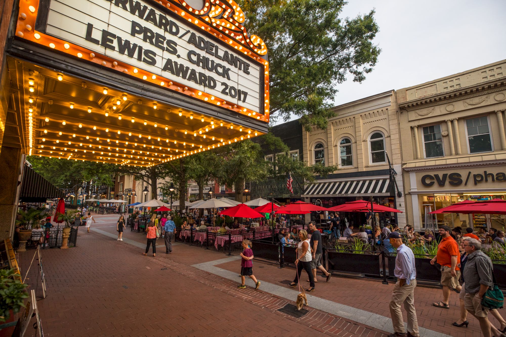 A lively outdoor shopping street with glowing lights, a neon marquee sign reading &ldquo;Hardy&hellip;&rdquo; and &ldquo;Lewis/Lewis,&rdquo; and people walking by.