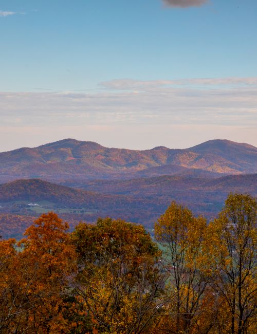 Autumn mountain valley landscape with layered ridges, blue sky, scattered clouds, and trees glowing in fall colors.