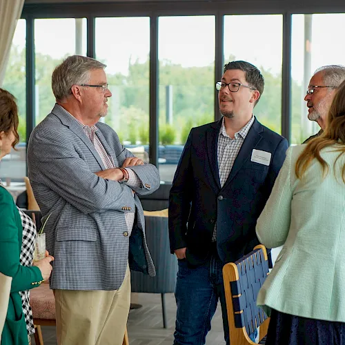 A group of people in a bright meeting room are talking and networking, exchanging ideas and smiles.