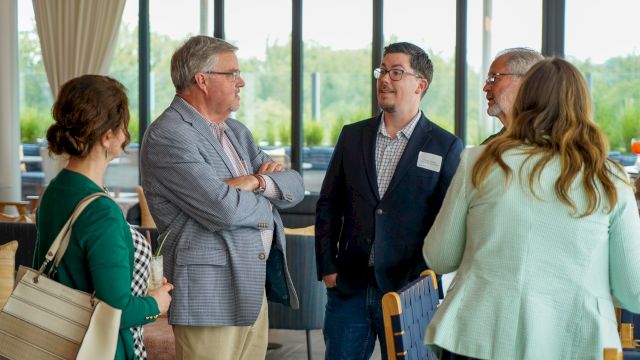 A group of people in a bright meeting room are talking and networking, exchanging ideas and smiles.