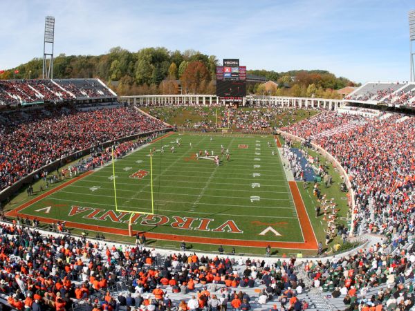 A packed Virginia Tech football stadium with fans in orange and maroon and players on the field.