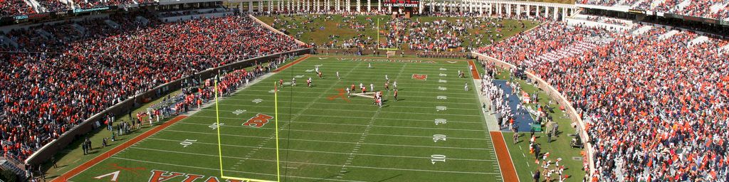 Packed American football stadium with Virginia Tech colors, teams on the field, and massive crowds in both grandstands.