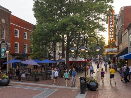 A lively outdoor shopping street with brick buildings, umbrellas, people strolling, and a tall Harmazing sign catching sunset light.