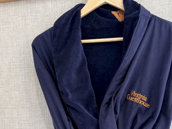 A navy bathrobe is hanging on a wooden hanger against a wall with coat-stand hooks above.