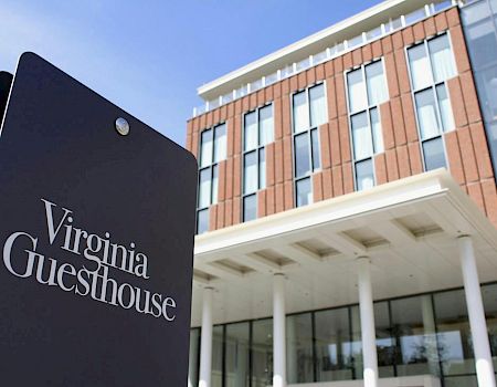 A dark sign reading “Virginia Guesthouse” in front of a modern brick hotel building with white columns.